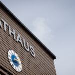 Frontseite des Rathauses Parkstetten, Aussenfassade mit braunen Holz verkleidet, darauf eine große Uhr und darüber ist mit großen silbernen Buchstaben Rathaus zu lesen.