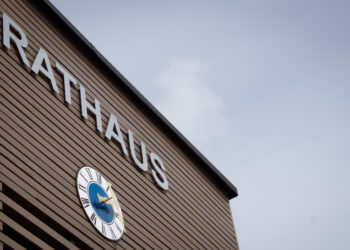 Frontseite des Rathauses Parkstetten, Aussenfassade mit braunen Holz verkleidet, darauf eine große Uhr und darüber ist mit großen silbernen Buchstaben Rathaus zu lesen.